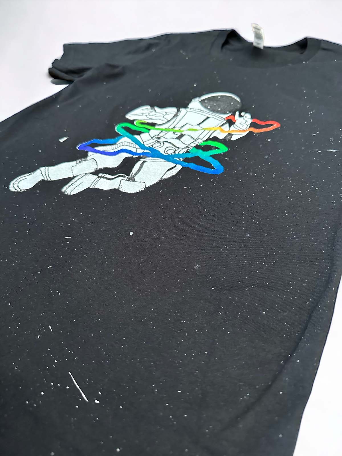close up side view of a vintage black t-shirt speckled with paint featuring a rainbow gay astronaut graphic