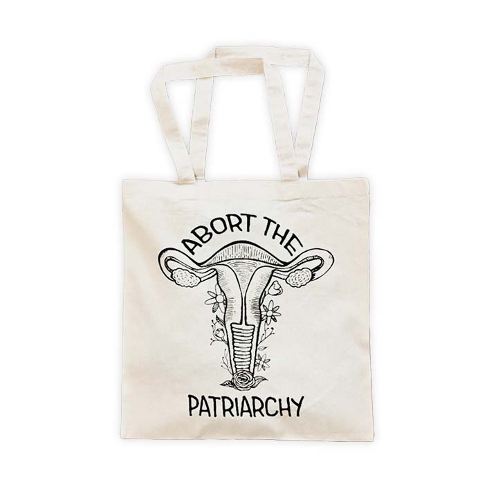 natural canvas tote with a black screen printed floral uterus graphic and "abort the patriarchy" text