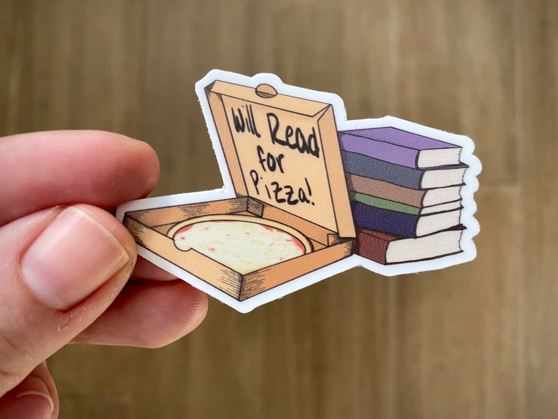 hand holding a sticker showing a pizza box with a stack of books with text "will read for pizza" 