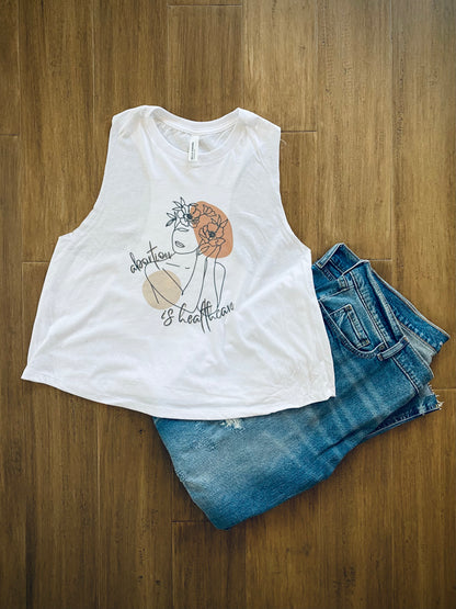 white crop top with a woman line drawing and abortion is healthcare text displayed with a pair of jeans on a light wood background